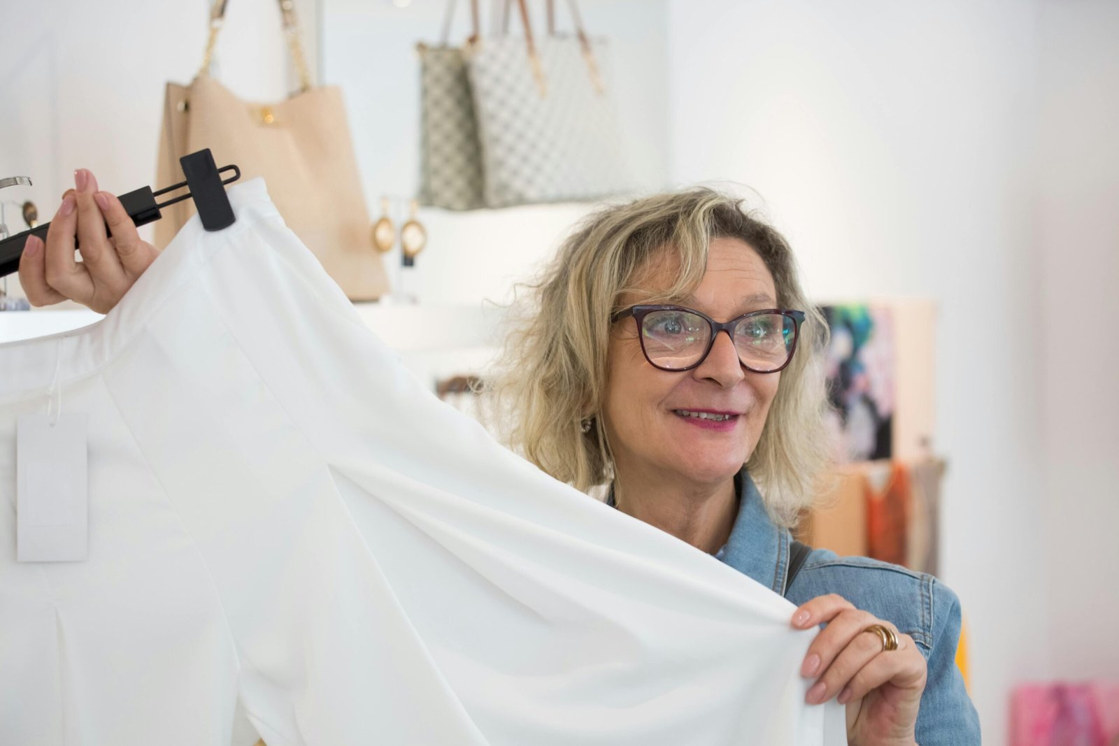 Elderly woman enjoying shopping in a boutique, holding a white garment with joy.